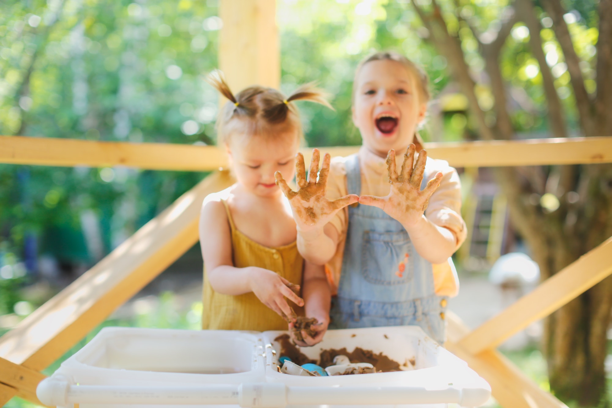 Happy children play with sand and water in sensory baskets on the outdoor sensory table,